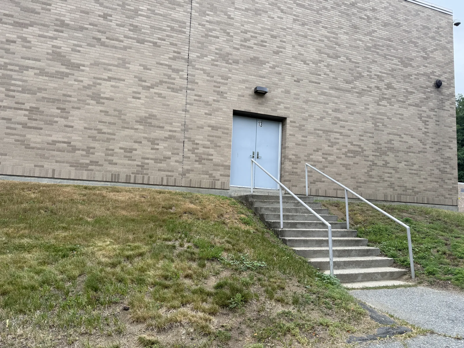 Plain poured-concrete exterior service staircase with a metal pipe handrail leading up to a doorway numbered 13 at the rear of the brick Harrington Building.