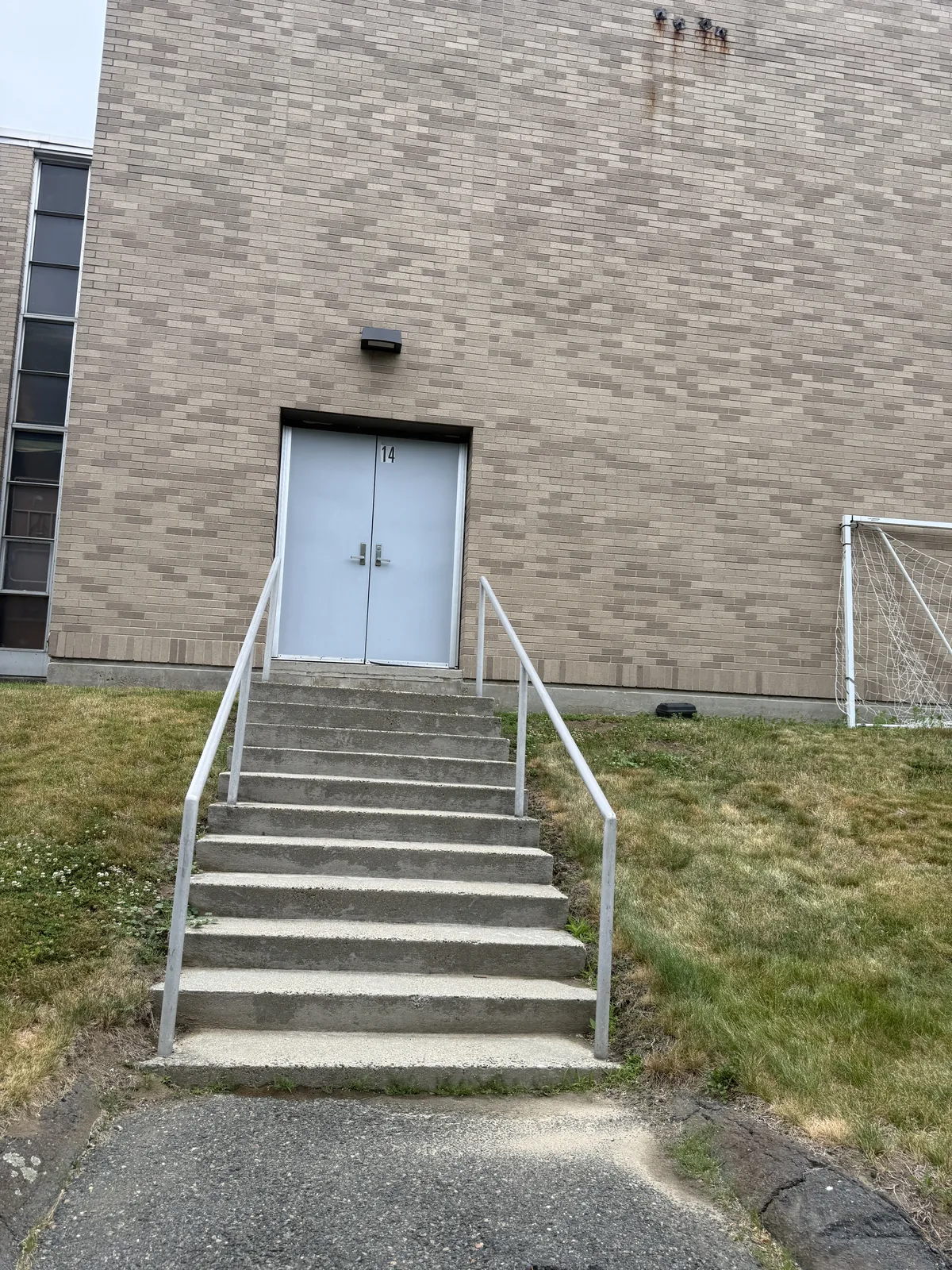 A second plain concrete exterior service staircase with a metal pipe handrail leading up to a doorway numbered 14 at the rear of the Harrington Building.